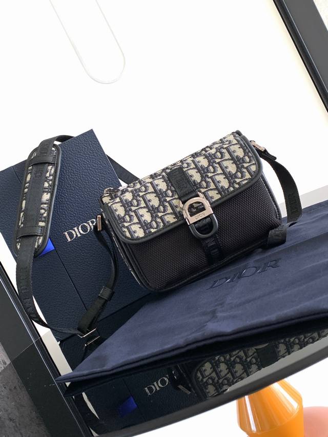 这款 Dior 8 手袋附有肩带 于二零二三秋季男装系列全新推出 别具一格的设计彰显现代魅力和简约美学 采用米色和黑色 Oblique 印花面料精心制作 刚性设