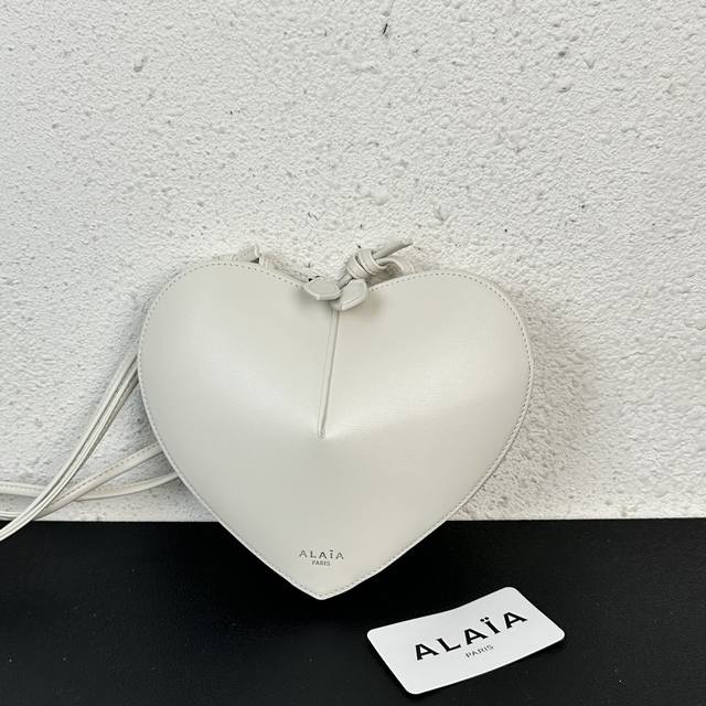 Alaia Coeur Bag 爱心手袋系列，立体爱心设计辨识度超高，拉链袋配有可调式的肩带，非常适合携带必需品，造型简洁，包包印有精致的 Logo 银色浮雕标
