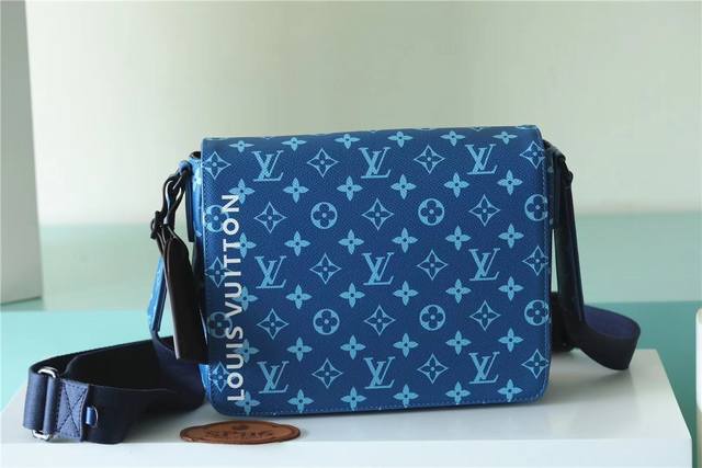 顶级原厂 m23785 蓝色District PM邮差包由帆布制成，带有字母组合图案，包正面印有白色大号的“Louis Vuitton”。磁性翻盖闭合和背面的拉